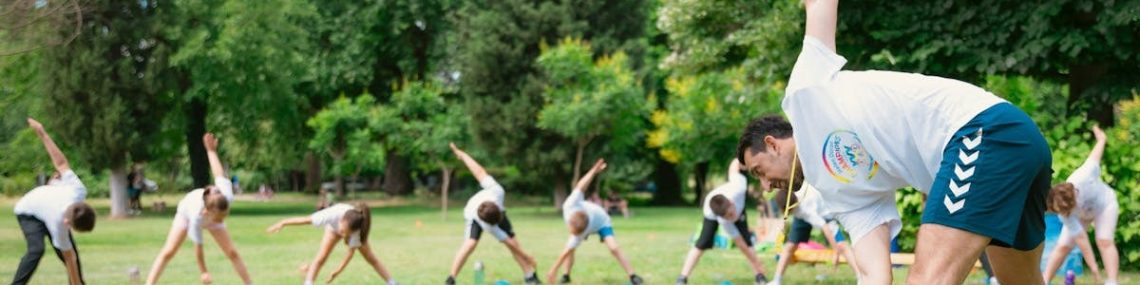 Kids stretching exercises in a park guided by a coach, promoting fitness and fun.