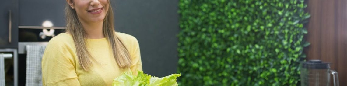 A cheerful woman in a modern kitchen presenting a fresh vegetable salad.